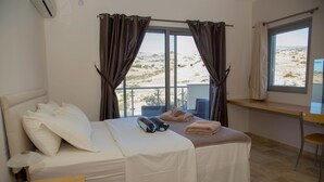A hotel room with a bed, a small table, a chair, and a window with curtains. - Rejuvenate family & friends at Stunning Villa Estia - close to beach & tavernas. (Makry Gialos)