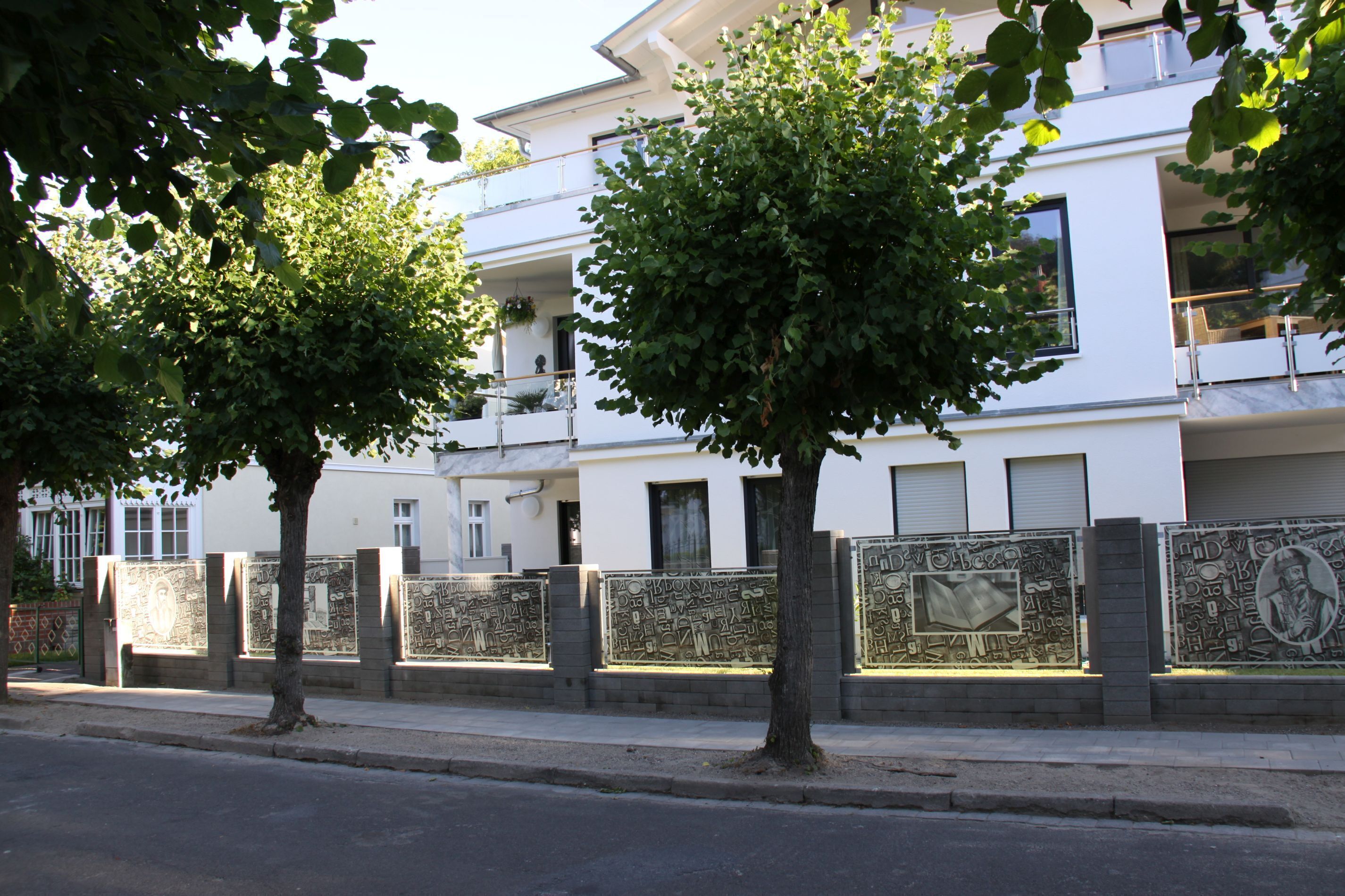 Un bâtiment moderne à la façade blanche, doté de nombreux balcons et d’un mur décoratif orné de motifs complexes.