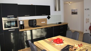 Una cuina moderna amb armaris negres, una campana extractora d'acer inoxidable i una taula de dinar de fusta amb caires.