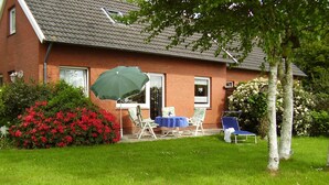 Une maison en briques avec un toit en tuiles, une terrasse avec une table et des chaises, et un grand parasol vert.