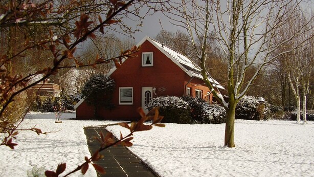 Une maison en briques rouges, avec une pelouse recouverte de neige et un chemin menant à l’entrée.