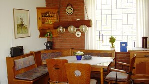 Un coin repas chaleureux avec un mur en briques, des meubles en bois et une fenêtre agrémentée de rideaux blancs.