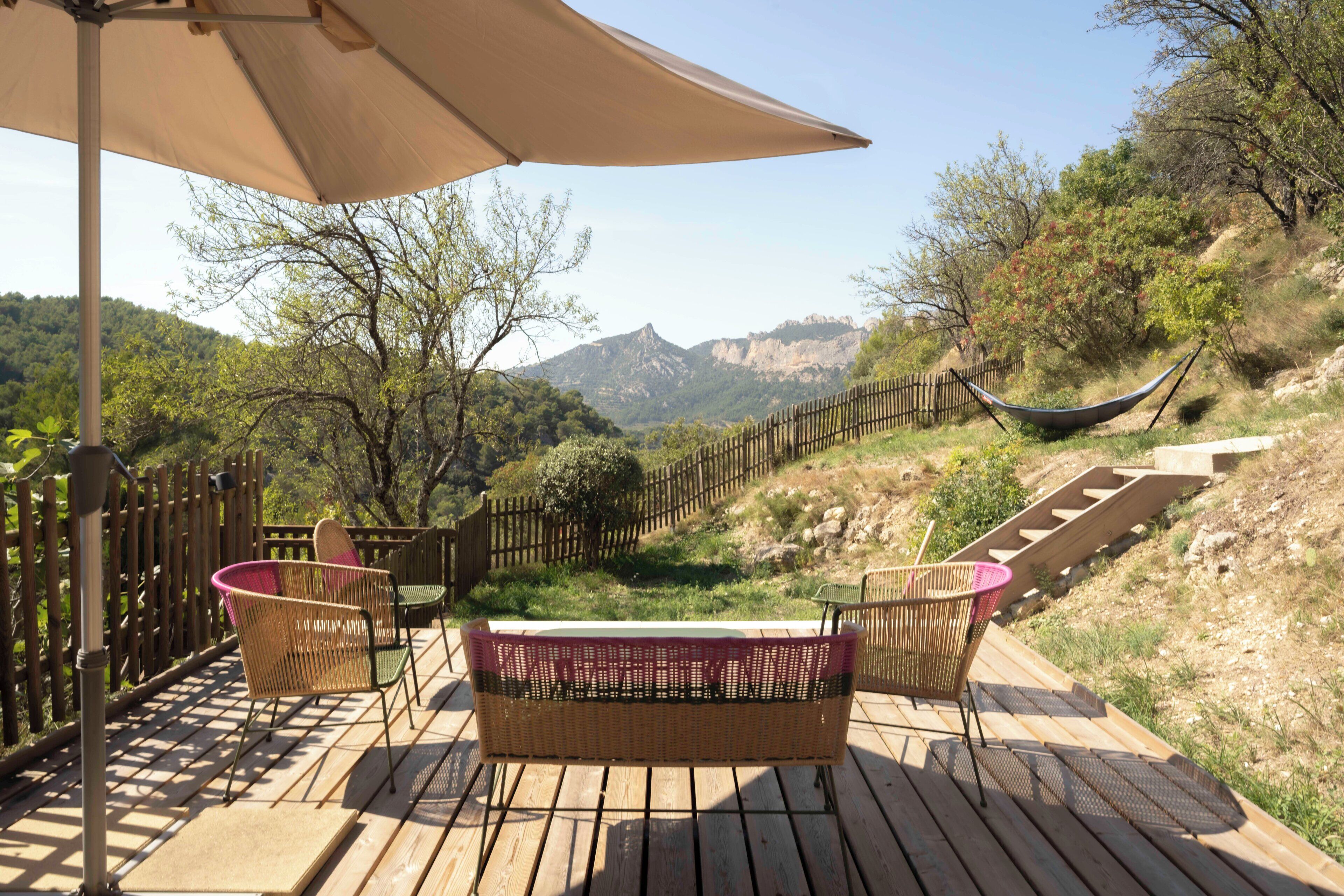 A wooden deck with wicker furniture and a hammock, overlooking a mountainous landscape.