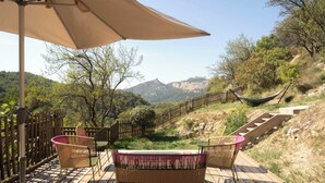 Une terrasse en bois, agrémentée de meubles en osier et d’un hamac, qui offre une vue sur un paysage montagneux.