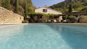 Une piscine aux eaux cristallines, bordée d’un côté par un mur de pierre et, en arrière-plan, un bâtiment avec un jardin.
