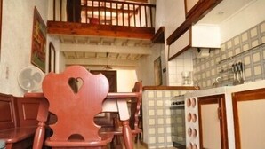 Un coin repas avec des chaises et une table en bois, une cuisine avec des meubles blancs et un dosseret carrelé, et un escalier avec des rampes en bois.