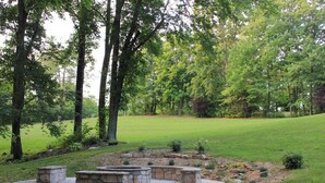 A circular stone seating area surrounded by a grassy field and trees.