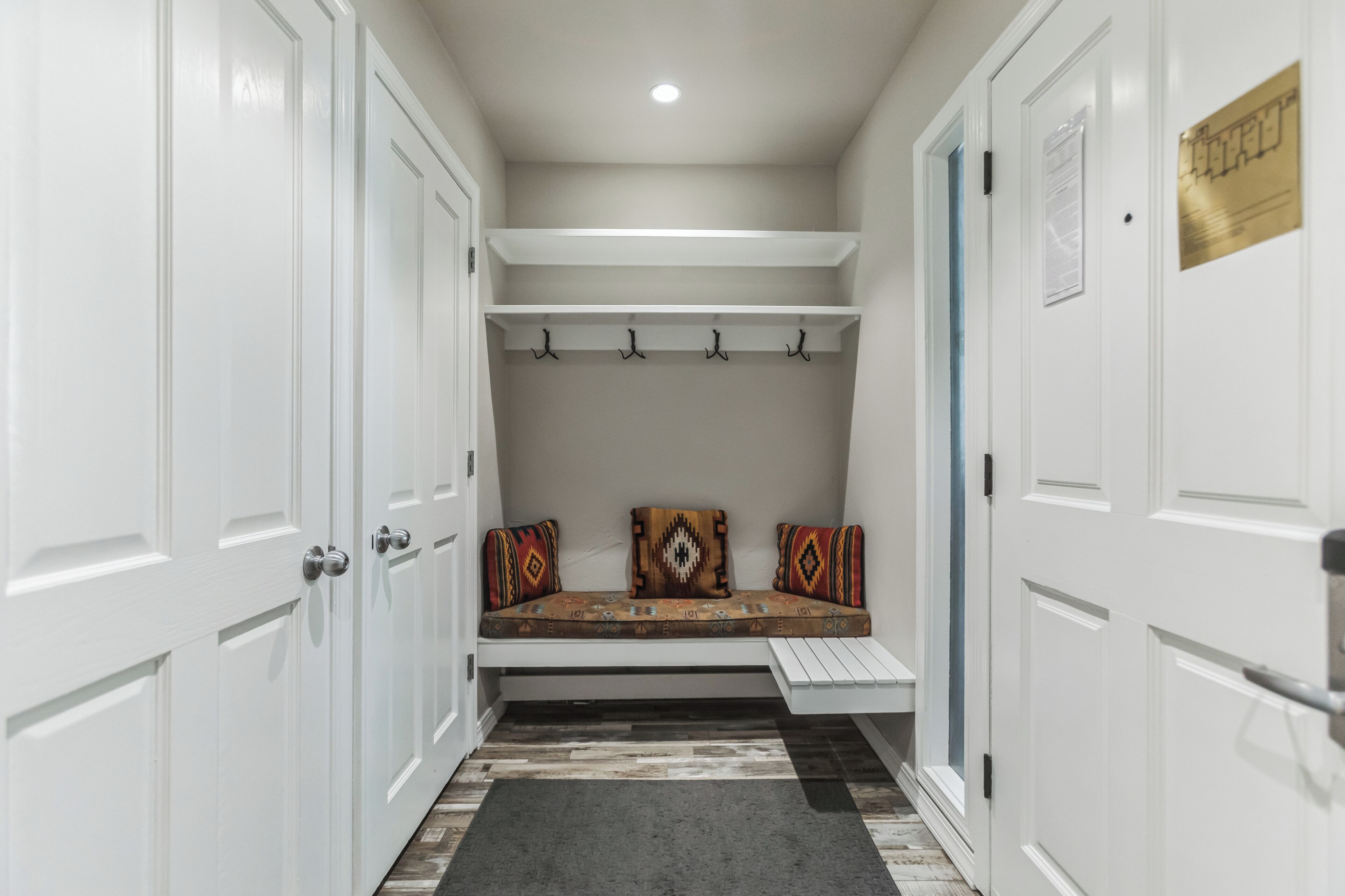 A hallway with white doors, a bench with patterned cushions, and a small shelf above.