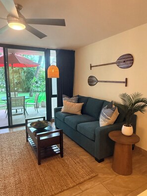 Ein Wohnzimmer mit einer Couch, einem Couchtisch, einem Deckenventilator und Blick auf einen Garten durch eine Schiebetür.