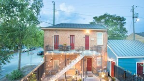 Un bâtiment à deux étages en briques, doté d’un balcon, d’un escalier et d’un espace extérieur aménagé pour s’asseoir.