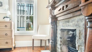 Une pièce avec une cheminée, une fenêtre avec des barreaux en métal, une chaise blanche et des meubles en bois.