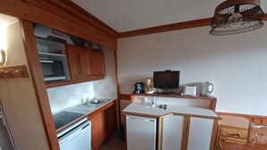 Cocina compacta con armarios de madera, microondas, cafetera, tostadora y un refrigerador pequeño.