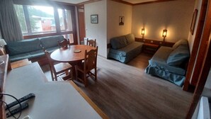 Una sala de estar acogedora con una mesa de madera, un sofá y un sillón. Hay dos lámparas de pared y un ventilador de techo.