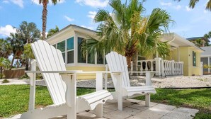 A patio area with two Adirondack chairs, a palm tree, and a yellow building with large windows. -  Easy one minute walk to #1 beach! (CLEARWATER BEACH)