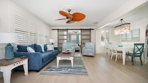A spacious living room with a blue sofa, a dining area with white chairs, and a ceiling fan. -  Easy one minute walk to #1 beach! (CLEARWATER BEACH)