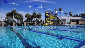 A swimming pool with multiple lanes, a water slide, and palm trees in the background. -  Easy one minute walk to #1 beach! (CLEARWATER BEACH)