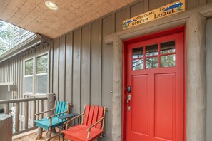 Ein Holzhaus mit roter Tür, einem Willkommensschild und zwei Adirondack-Stühlen.