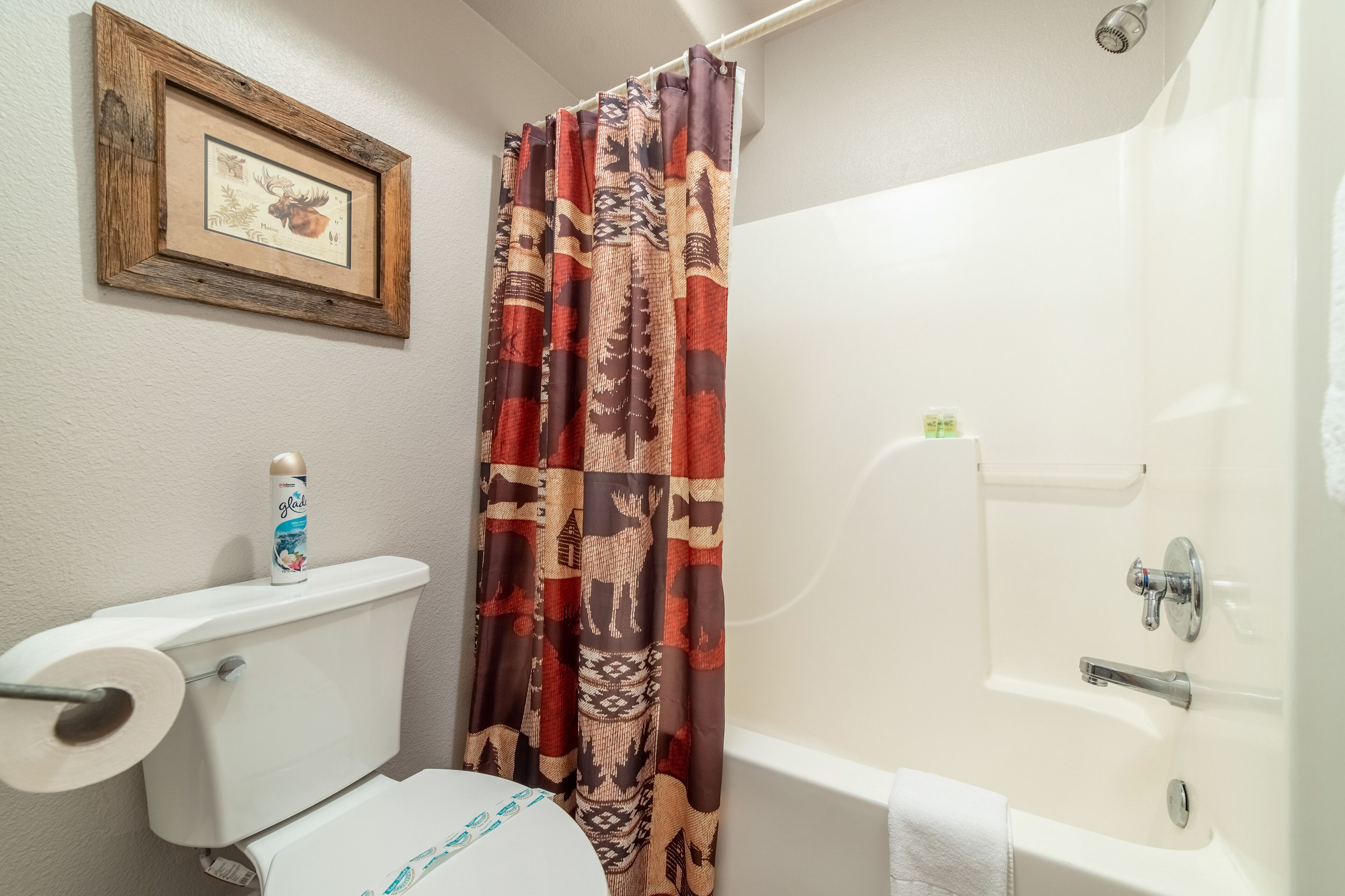 Un baño con inodoro, cortina de ducha, un cuadro en la pared y bañera.