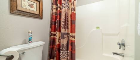 Un baño con inodoro, cortina de ducha, un cuadro en la pared y bañera.