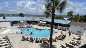 A pool area with lounge chairs and a palm tree. - 30 Steps to the Beach! Luxury Condo with Large wrap-around porch! (Tybee Island)