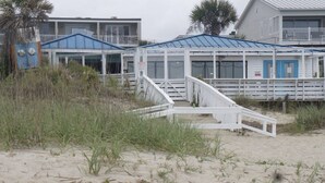 A beachfront building with a blue roof, white exterior, and a white staircase leading to the entrance. - 30 Steps to the Beach! Luxury Condo with Large wrap-around porch! (Tybee Island)