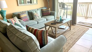 A living room with a grey sofa, colorful pillows, a coffee table, and a lamp. - 30 Steps to the Beach! Luxury Condo with Large wrap-around porch! (Tybee Island)