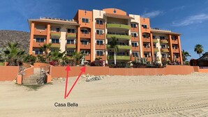 Un hôtel à plusieurs étages doté de balcons, situé en bord de plage, avec une plage de sable fin et des palmiers.