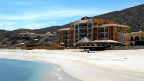 Un hôtel situé en bord de mer, doté de nombreux balcons, d’une plage de sable et offrant une vue sur un paysage montagneux.