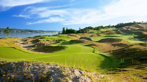 Een golfbaan met zandbunkers, een waterpartij en een bebost gebied op de achtergrond.