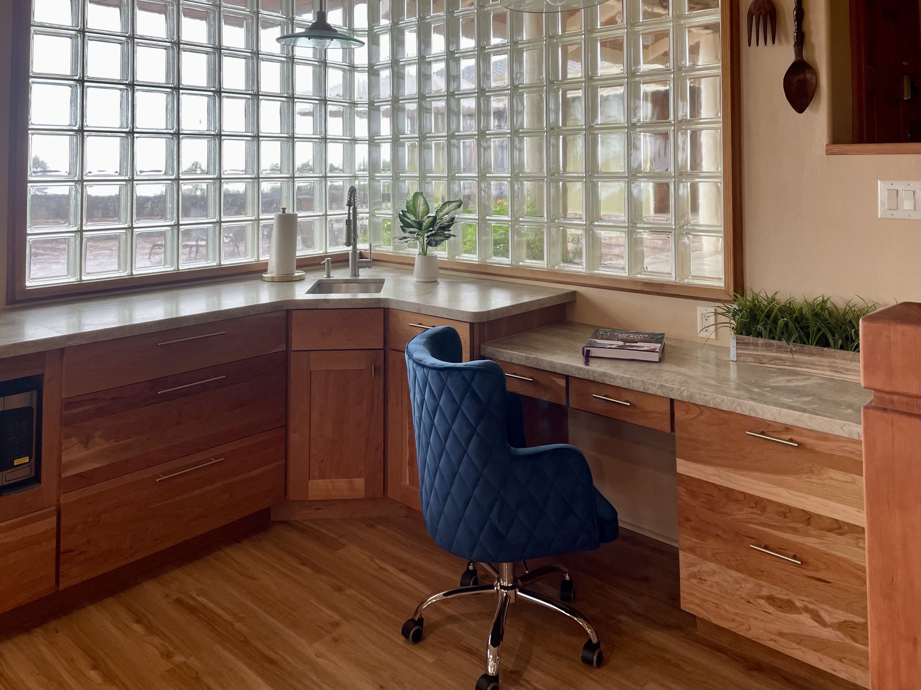 A kitchen with wooden cabinets, a blue chair, a sink, and a window with a view.