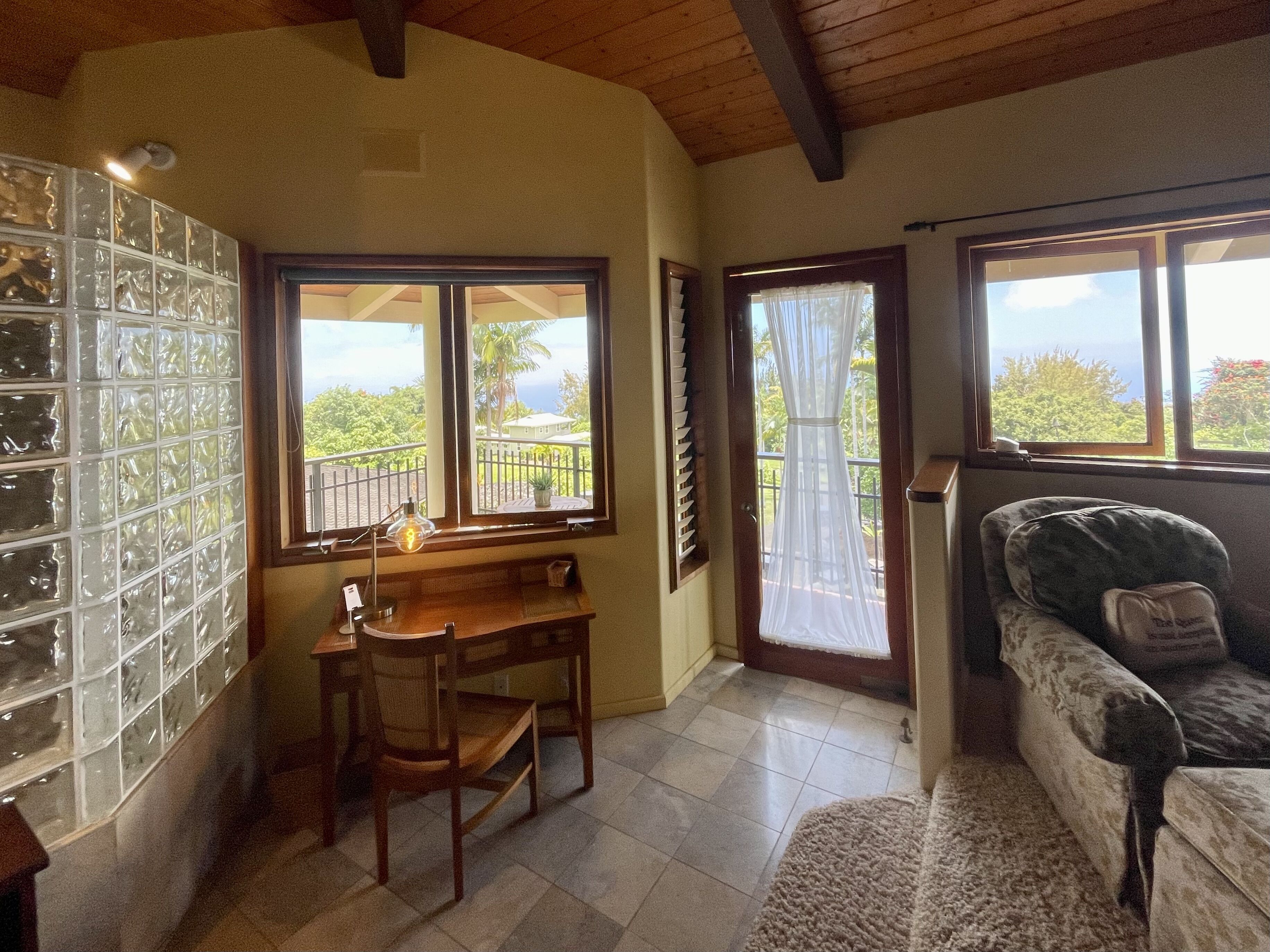 A room with a dining table and chairs, a sofa, and large windows offering a view of the outdoors.