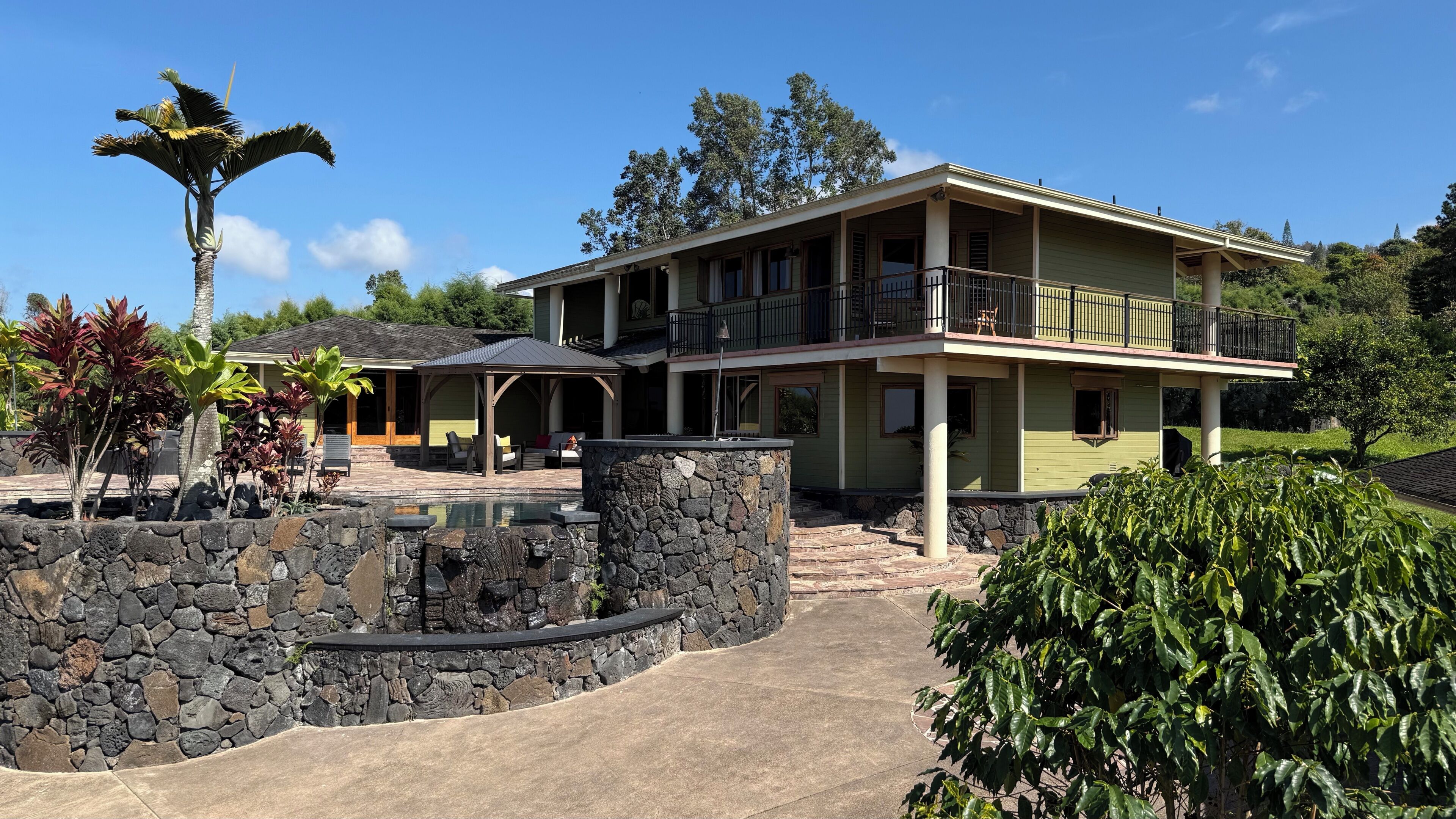 A two-story house with a stone pool, outdoor seating, and a covered patio.