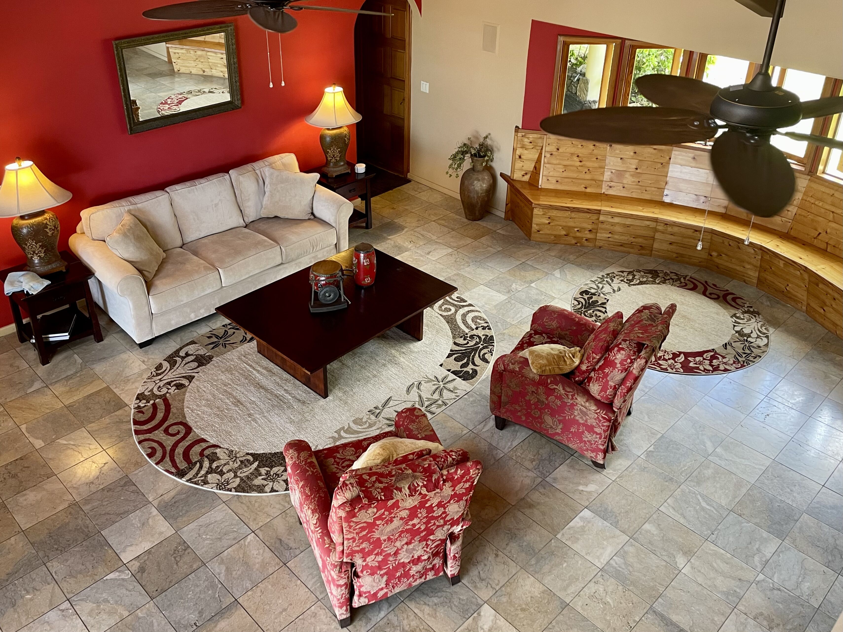 A living room with a beige sofa, a red floral armchair, a wooden coffee table, and a patterned rug.