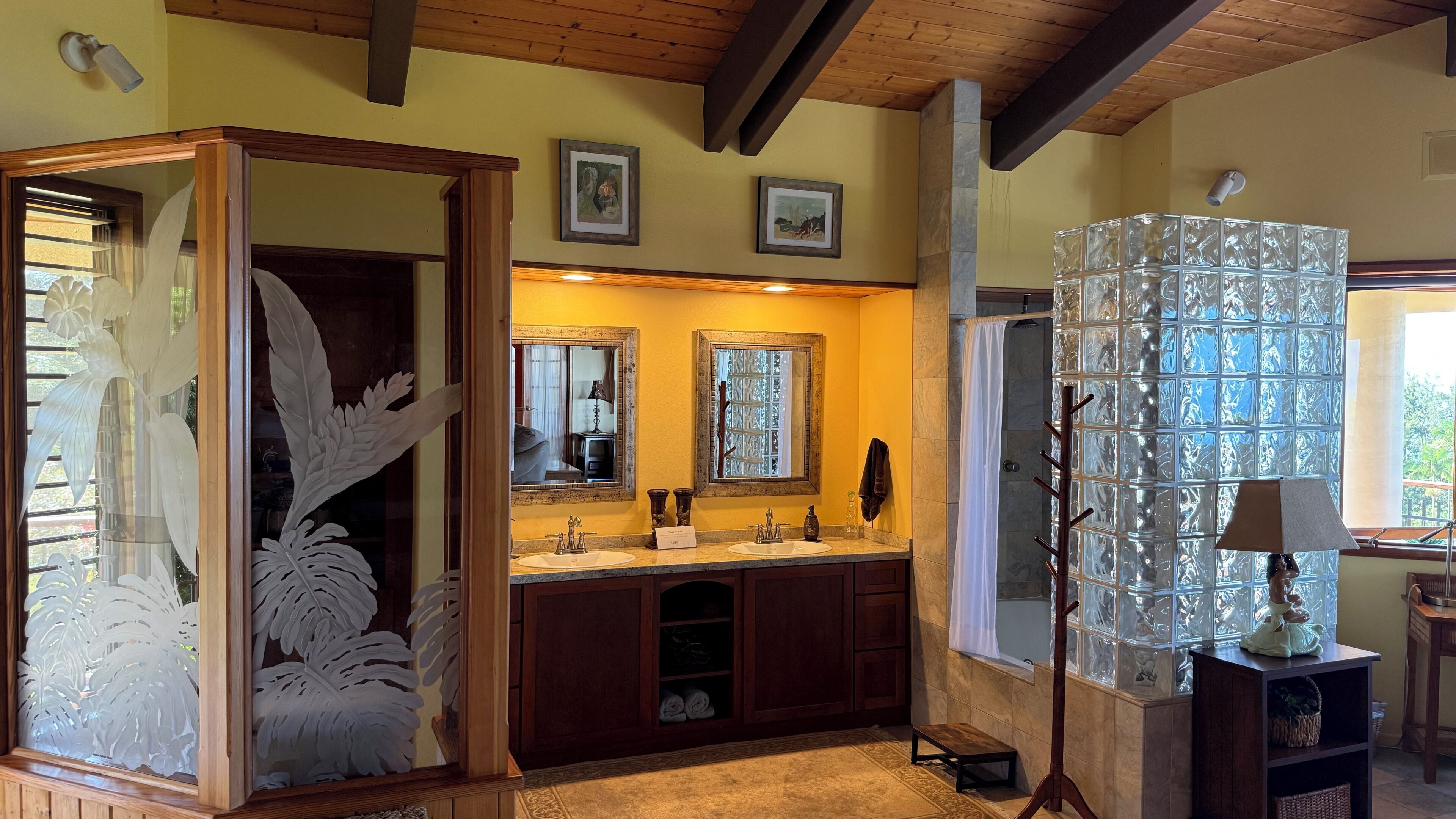 A bathroom with a wooden vanity, two mirrors, a glass shower enclosure, and a decorative plant.