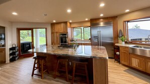 Une cuisine moderne dotée d’un grand îlot central, de meubles en bois, d’appareils électroménagers en acier inoxydable et offrant une vue sur l’extérieur.