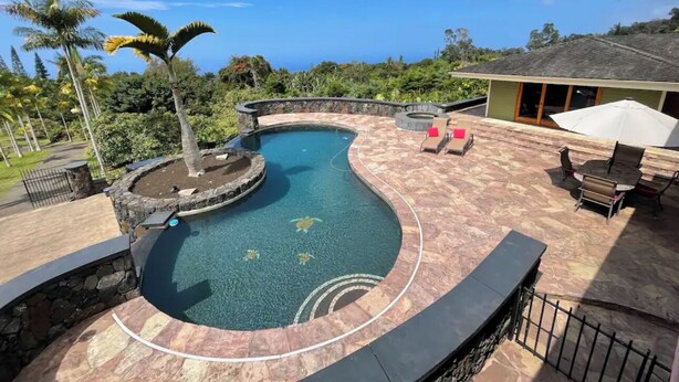 Une piscine au design incurvé, entourée d’une terrasse en pierre et d’un espace patio aménagé avec du mobilier d’extérieur.