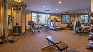 Een sportschool met diverse fitnessapparaten, waaronder loopbanden, krachttrainingsapparaten en een bank.