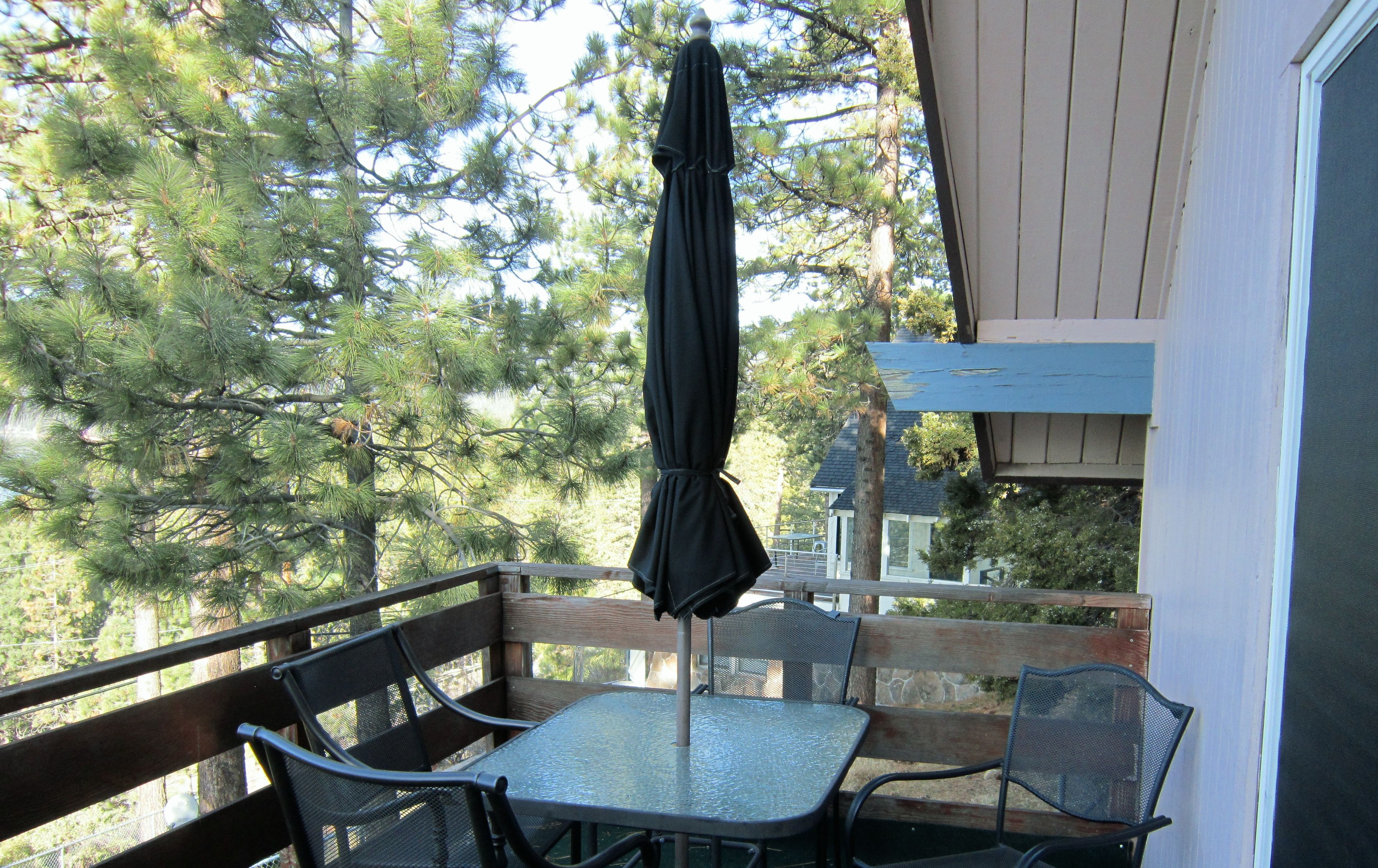A balcony with a table and chairs, an umbrella, and a view of trees.