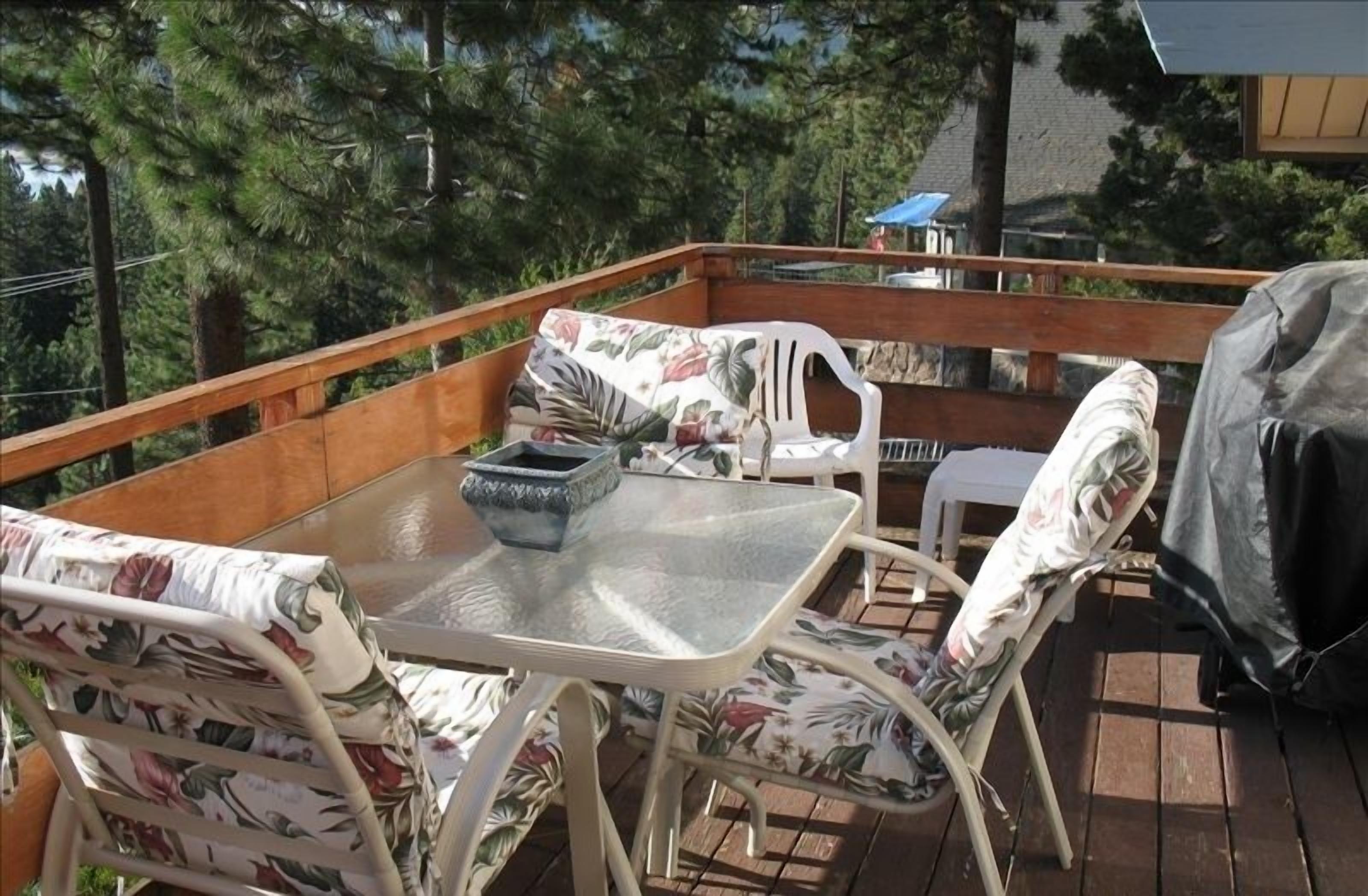 A wooden deck with a glass table and floral-patterned chairs.