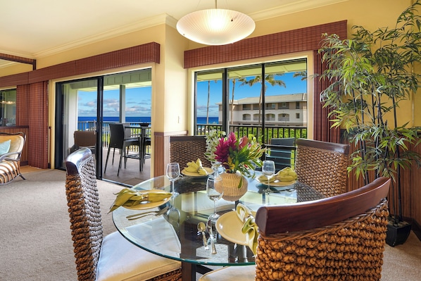 A dining area with a glass table, wicker chairs, and a view of the ocean.