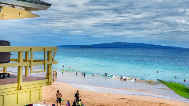 Una playa con una torre de salvavidas, cielos despejados y aguas tranquilas.