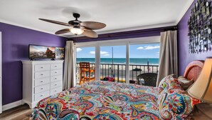 Une chambre avec un grand lit, un ventilateur de plafond, une commode et une vue sur la plage.