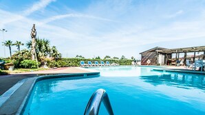 Une piscine avec un poste de surveillance pour les sauveteurs, des chaises longues et un palmier en arrière-plan.