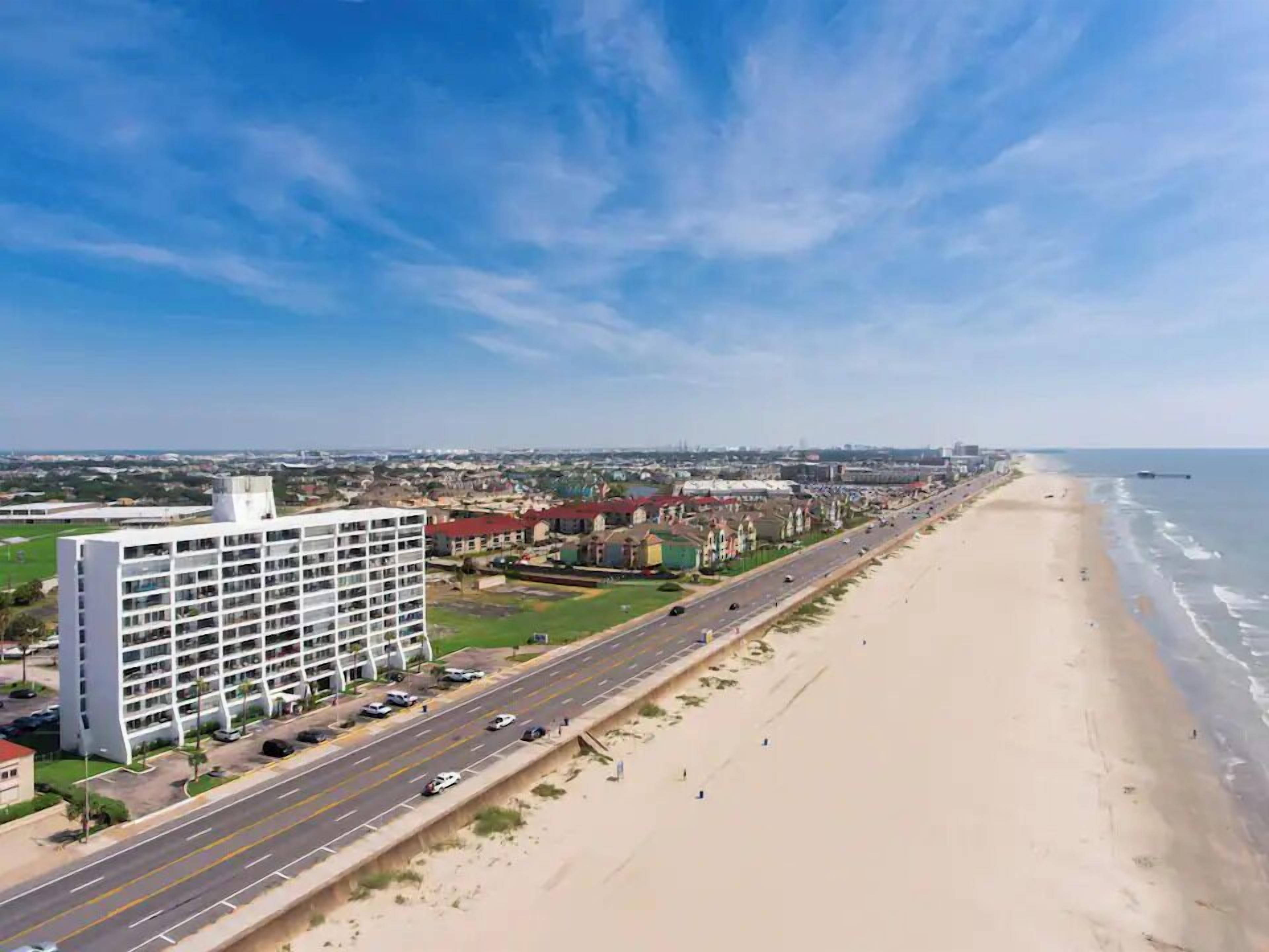 A coastal cityscape with a prominent white hotel, a wide road, and a beach.