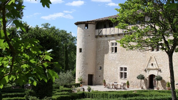 A stone building with a tower, surrounded by a well-maintained garden and outdoor seating area. - Château de Mayragues (Cahuzac-sur-Vere)