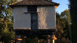 A small, rustic building with a tiled roof and a central door, supported by stone pillars, set in a grassy area with trees in the background. - Château de Mayragues (Cahuzac-sur-Vere)