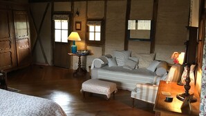 A cozy room with a wooden floor, a sofa, a table with a lamp, and a bed with floral bedding. - Château de Mayragues (Cahuzac-sur-Vere)