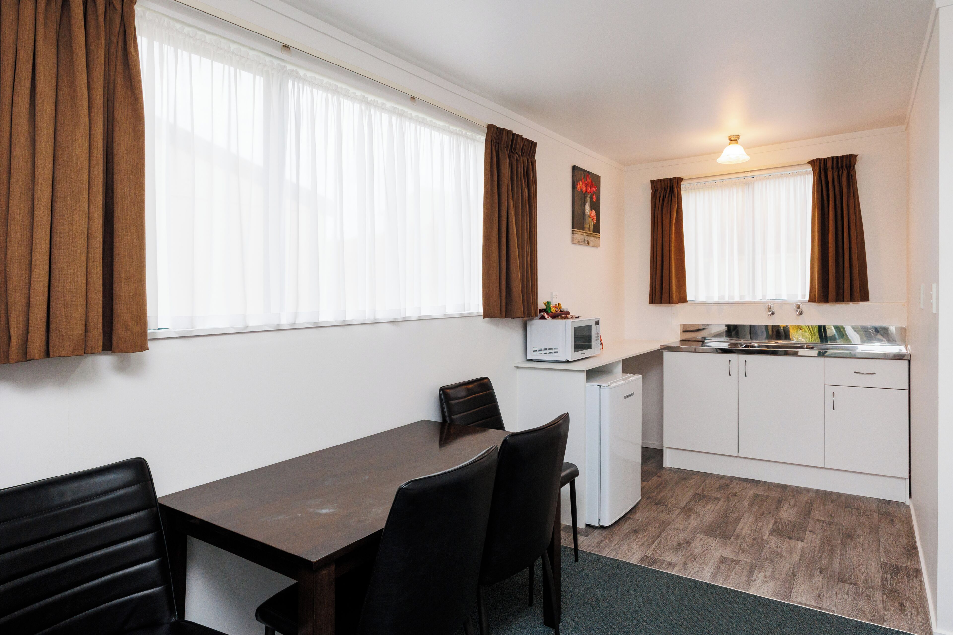 A compact kitchen with a dining area, white cabinets, a microwave, and a small refrigerator.