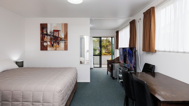 A hotel room with a bed, a desk, a chair, a television, and a painting on the wall.