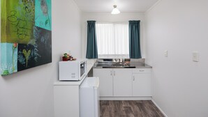 A compact kitchen with white cabinets, a microwave, a refrigerator, and a window with curtains.